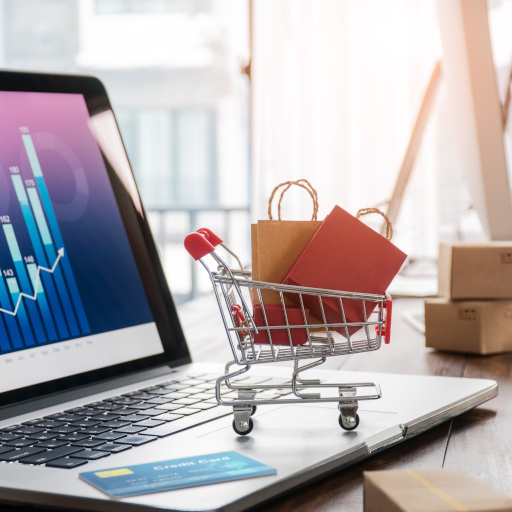 Shopping bags incart and credit card on laptop with paper boxes on table and sales data economic growth graph on screen, buying and selling services online on network, e-commerce concept