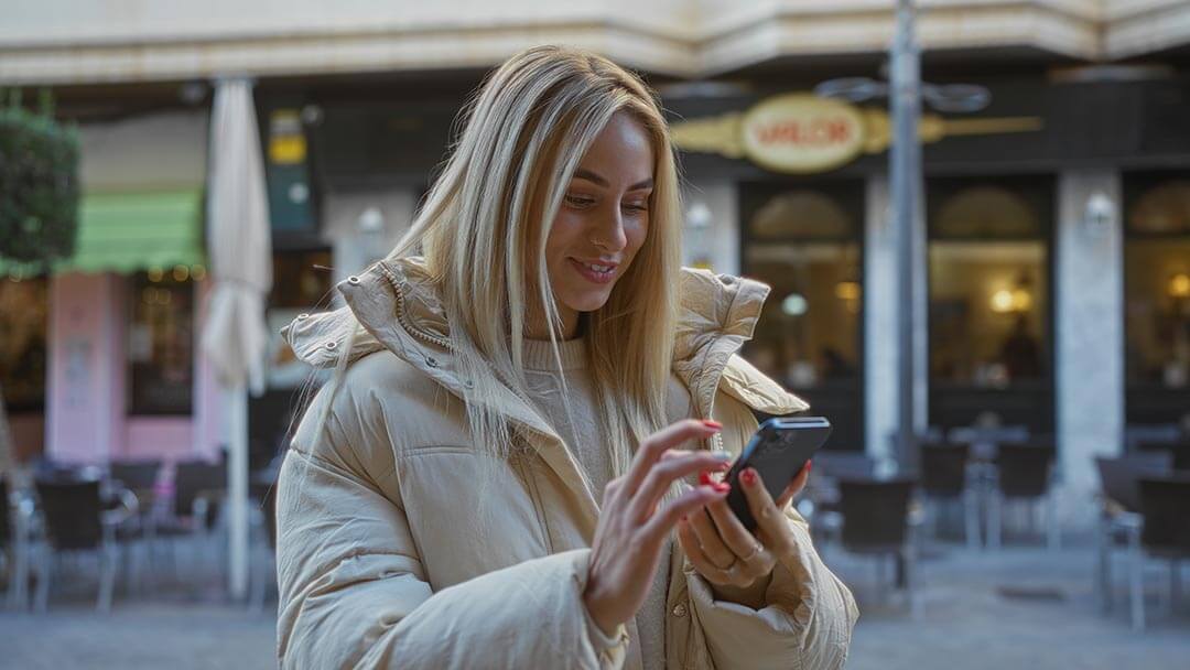 woman on street corner smiling and looking down at the screen